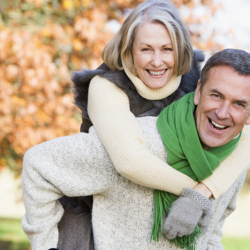 Senior man giving woman piggyback ride through autumn woods